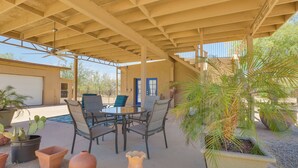 Une terrasse extérieure avec une table et des chaises, entourée de plantes en pot et dotée d’un ventilateur de plafond.