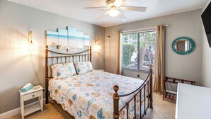 A bedroom with a bed, bedside table, nightstand, ceiling fan, window with curtains, and a wall-mounted mirror. - Relaxing Fort Myers Home w/ Screened-in Patio (Fort Myers)
