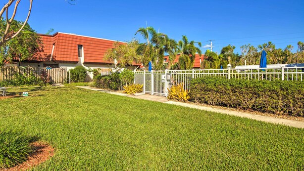 A residential property with a red-roofed house, a white fence, and a well-maintained lawn. - Relaxing Fort Myers Home w/ Screened-in Patio (Fort Myers)