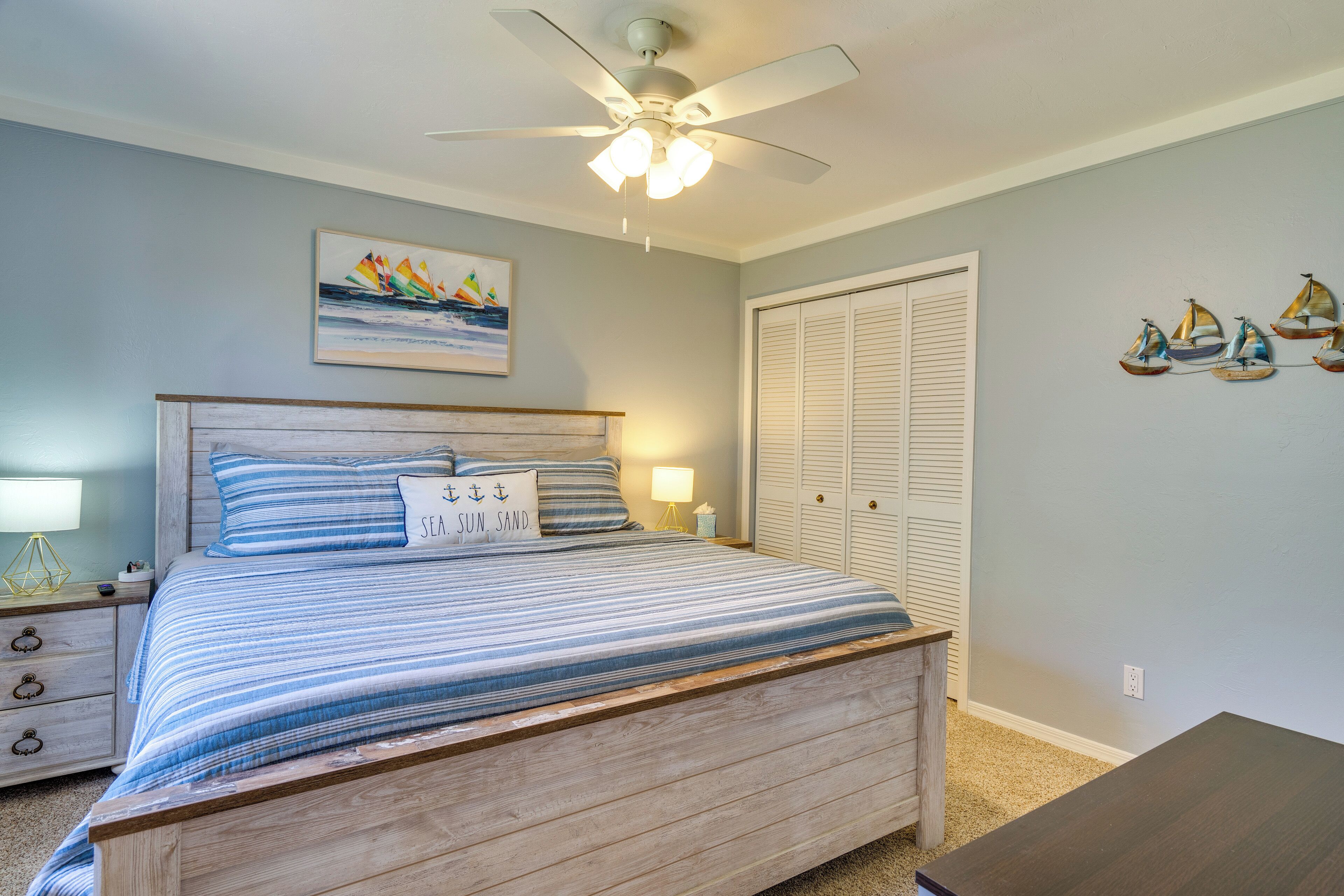 A bedroom with a bed, a nightstand, a ceiling fan, a wall-mounted painting, and a closet.
