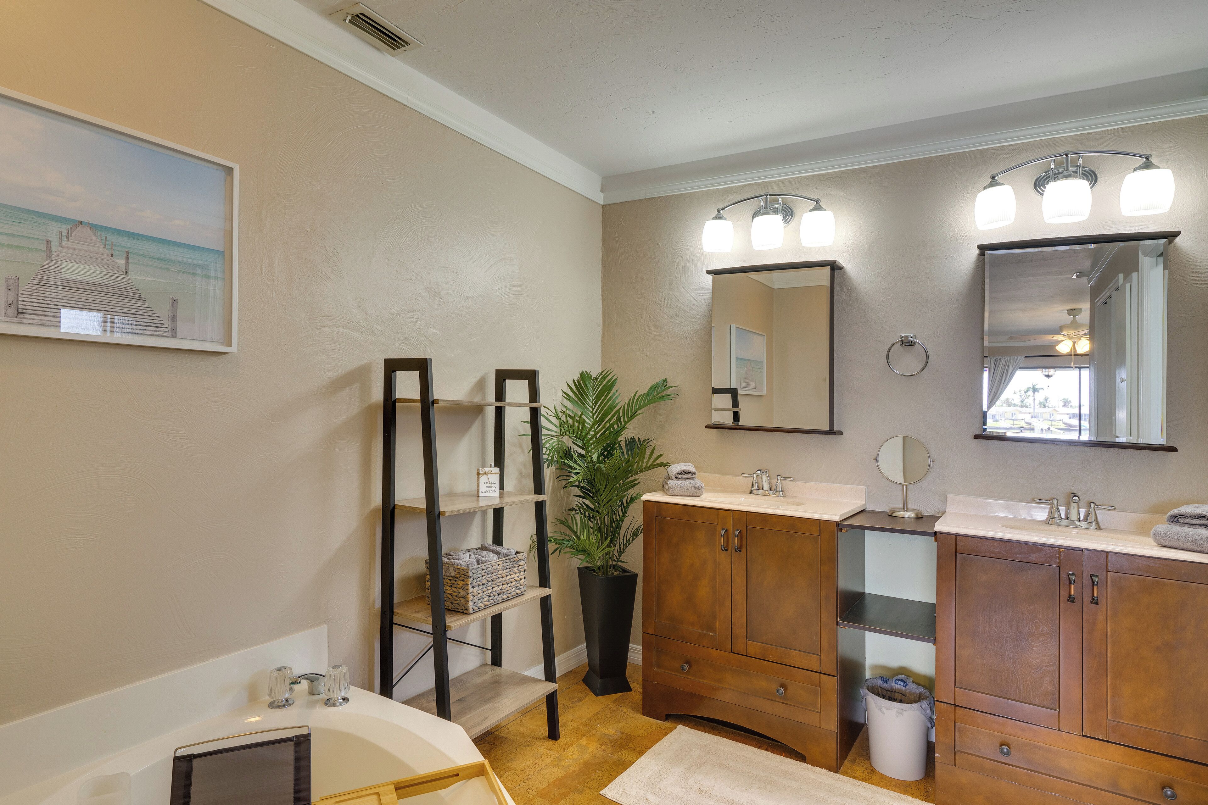 A bathroom with a wooden vanity, a large mirror, a potted plant, and a shelf with towels.