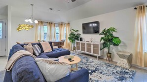 A modern living room with a blue sofa, a round coffee table, a ceiling fan, and a TV mounted on the wall. - Modern Granite Shoals Retreat w/ Fire Pit! (Marble Falls)