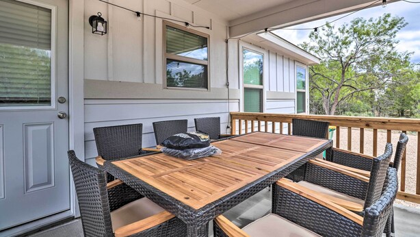 A covered patio with a wooden table and wicker chairs, a door with a window, and a view of trees. - Modern Granite Shoals Retreat w/ Fire Pit! (Marble Falls)