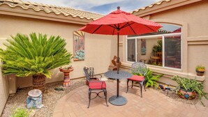 A patio with a round table and chairs, a red umbrella, and various potted plants. - Rustic Tucson Vacation Rental w/ Pool & Spa! (Saddlebrooke)