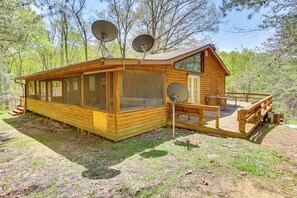 A wooden cabin with large windows, a deck, and satellite dishes. - Vacation Rental Near Hoosier National Forest! (Taswell)