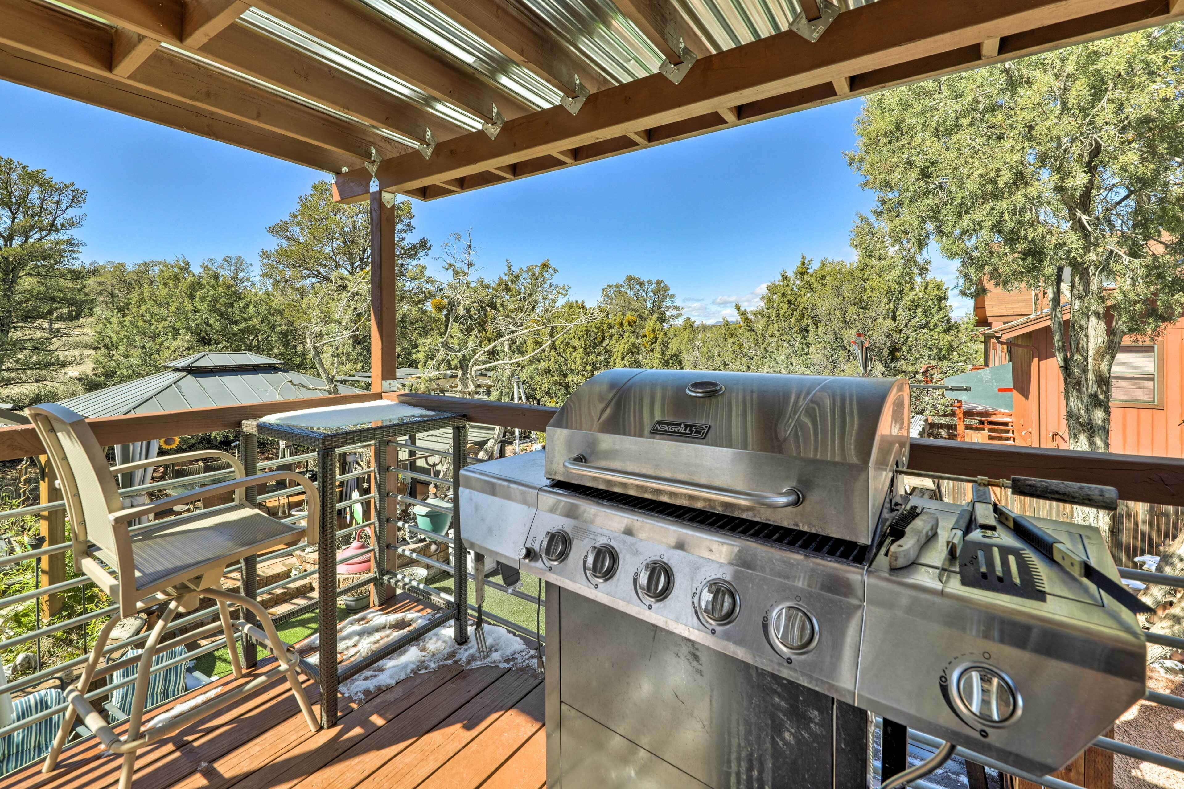 A covered outdoor area with a stainless steel grill, a table, and chairs.