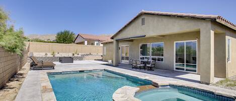A backyard with a swimming pool, patio furniture, and a covered seating area.