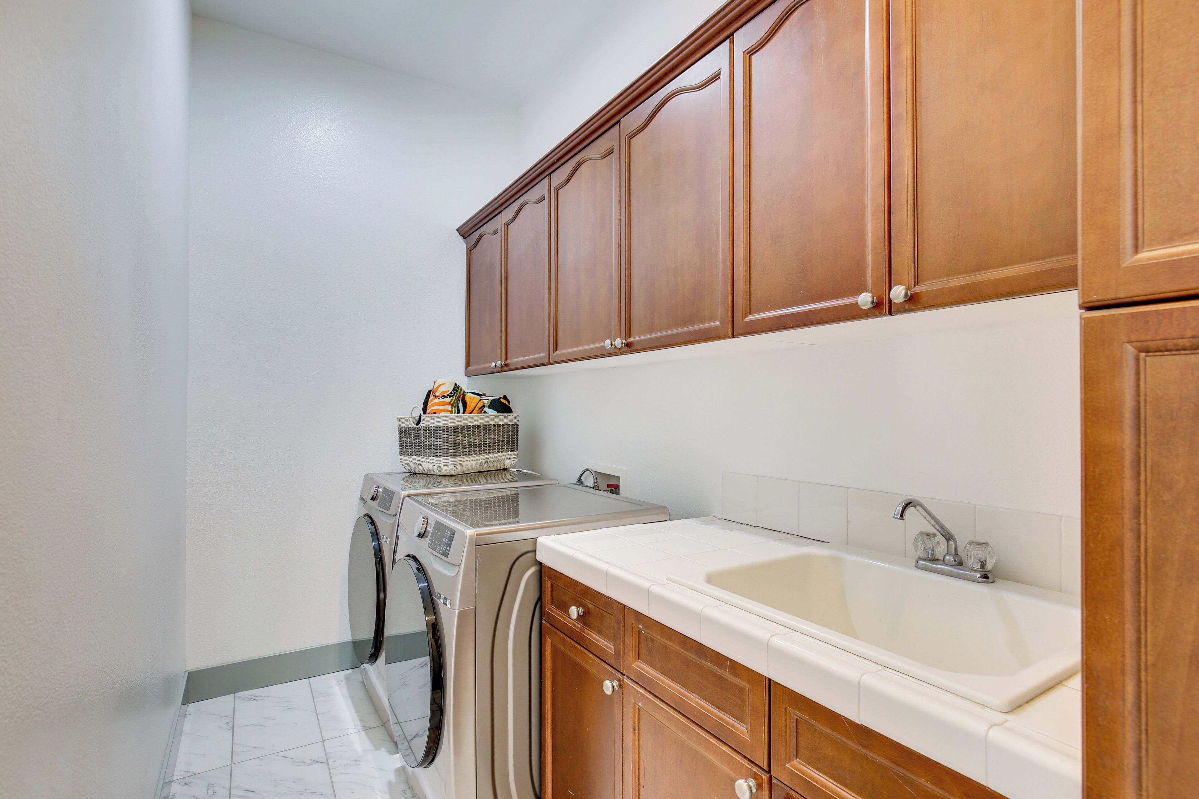 A laundry room with a washing machine, dryer, wooden cabinets, and a sink.