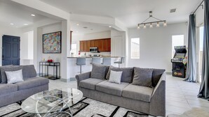 A modern living room with a grey sofa, a glass coffee table, and a kitchen in the background. - 'casa Del Sol' - Cozy Oasis in Desert Hot Springs! (Desert Hot Springs)