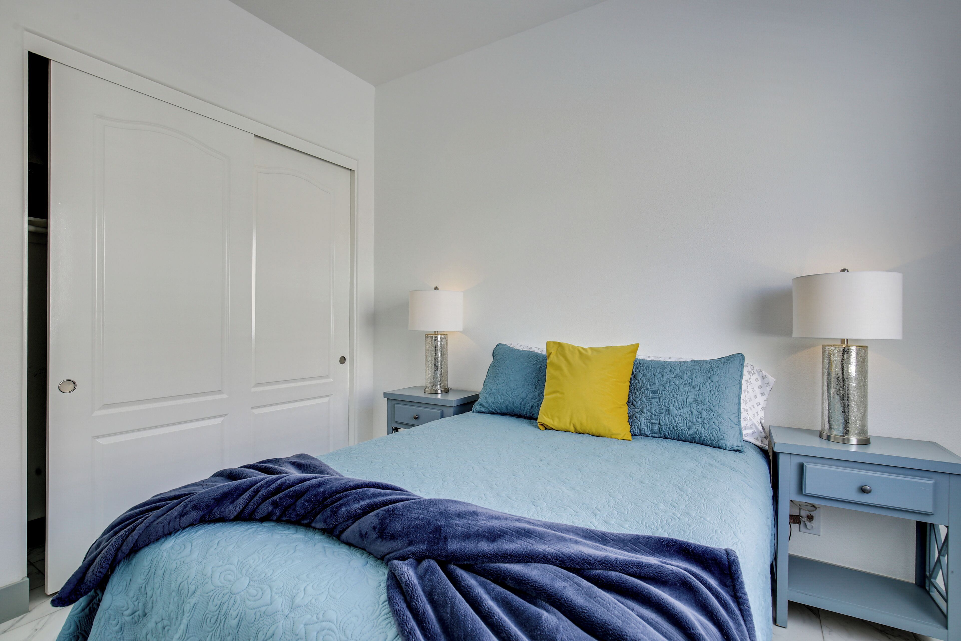 A bedroom with a bed, two bedside tables with lamps, a door, and a nightstand.