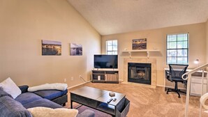 A living room with a sofa, coffee table, TV, fireplace, and a desk with a chair. - Gilbert Townhome w/ Easy Access to Phoenix! (Gilbert)
