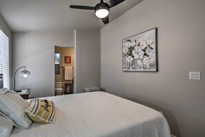 A bedroom with a bed, a ceiling fan, a nightstand, a lamp, and a painting on the wall.