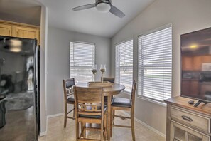 A kitchen with a refrigerator, wooden dining table, chairs, and a ceiling fan.