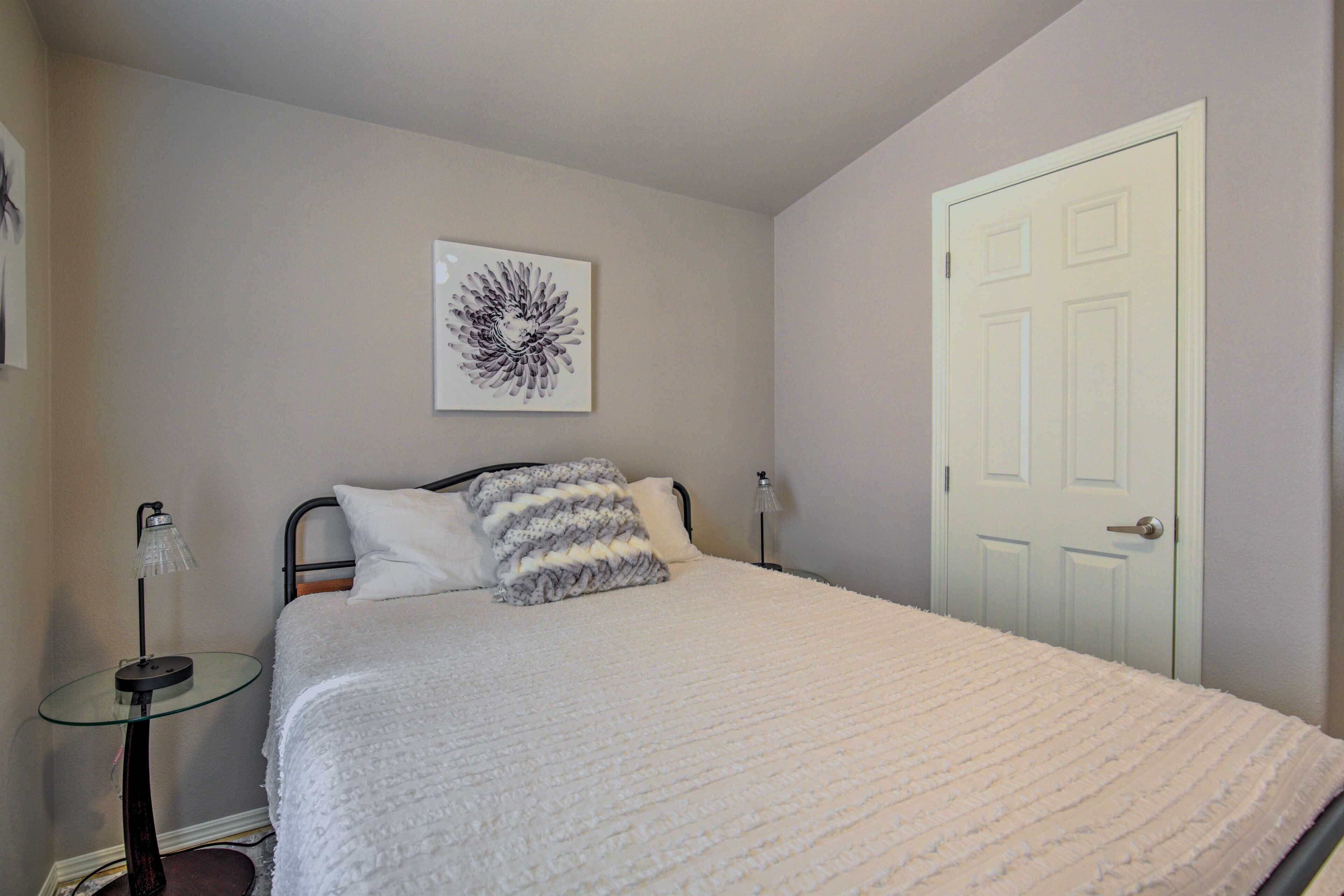 A bedroom with a bed, a bedside table with a lamp, a door, and a wall-mounted artwork.