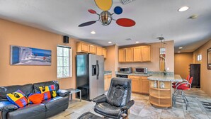 A living room with a black leather sofa, a black leather chair, and a small table. There is a kitchen area with wooden cabinets and a refrigerator. - Paradise Valley Cottage Near Hiking Trails! (Paradise Valley)