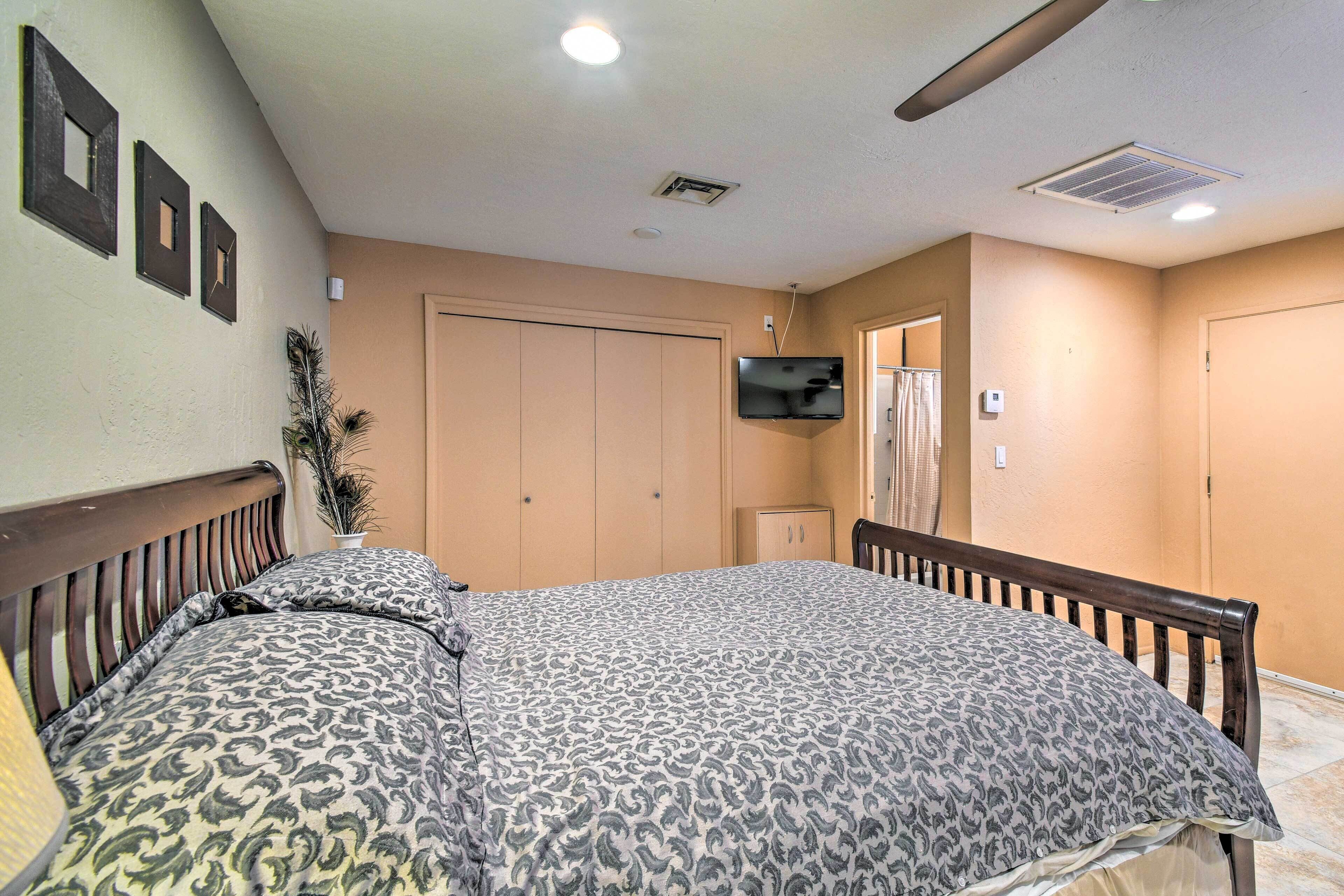 A bedroom with a bed, a TV mounted on the wall, and a door leading to another room.