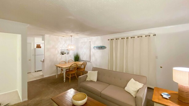 A living room with a sofa, coffee table, dining table, and chairs. There is a lamp on a side table. - Brigantine Condo w/ Gas Grill - Walk to Beach! (Brigantine)