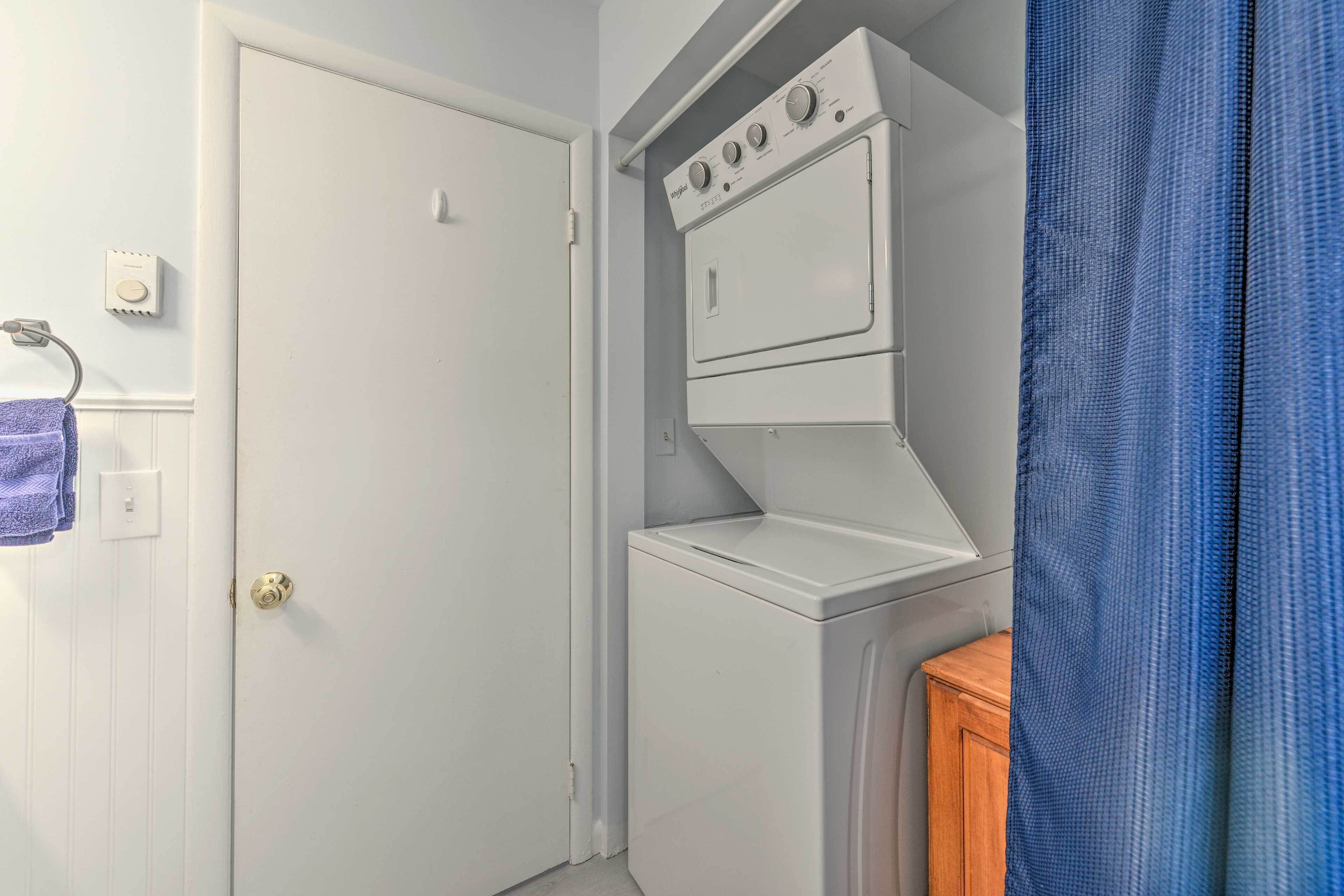 A laundry area with a stacked washer and dryer, a wooden cabinet, and a door with a towel hanging on a hook.