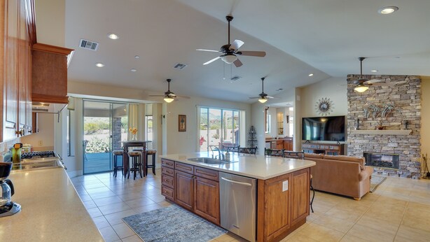 A spacious kitchen with a large island, wooden cabinets, and a built-in dishwasher. There are ceiling fans, a stone fireplace, and a large TV. - Hot Tub, Yard & Views: Spacious Cave Creek Home (Cave Creek)