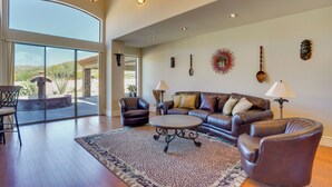 A spacious living room with a large window, leather furniture, and decorative wall art. - Hot Tub, Yard & Views: Spacious Cave Creek Home (Cave Creek)