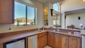 A modern kitchen with wooden cabinets, a built-in dishwasher, and a large window offering a view of the outdoors. - Hot Tub, Yard & Views: Spacious Cave Creek Home (Cave Creek)