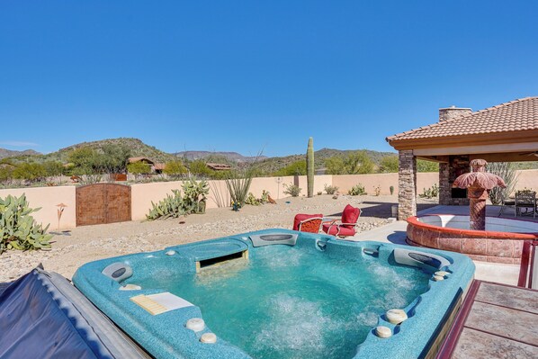 A hot tub with a stone structure, surrounded by desert plants and a clear blue sky. - Hot Tub, Yard & Views: Spacious Cave Creek Home (Cave Creek)