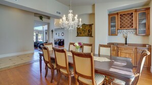 A dining room with a large wooden table, six chairs, and a chandelier. There is a kitchen area with wooden cabinets and a wine rack. - Hot Tub, Yard & Views: Spacious Cave Creek Home (Cave Creek)