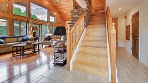 A spacious living room with a wooden staircase, large windows, and a cozy seating area. - Log Cabin in Payson w/ Deck, Mtn & Creek Views (Payson)