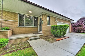 A residential house with a brick exterior, a front door, a garage, and a well-maintained front yard with a hedge and a tree.