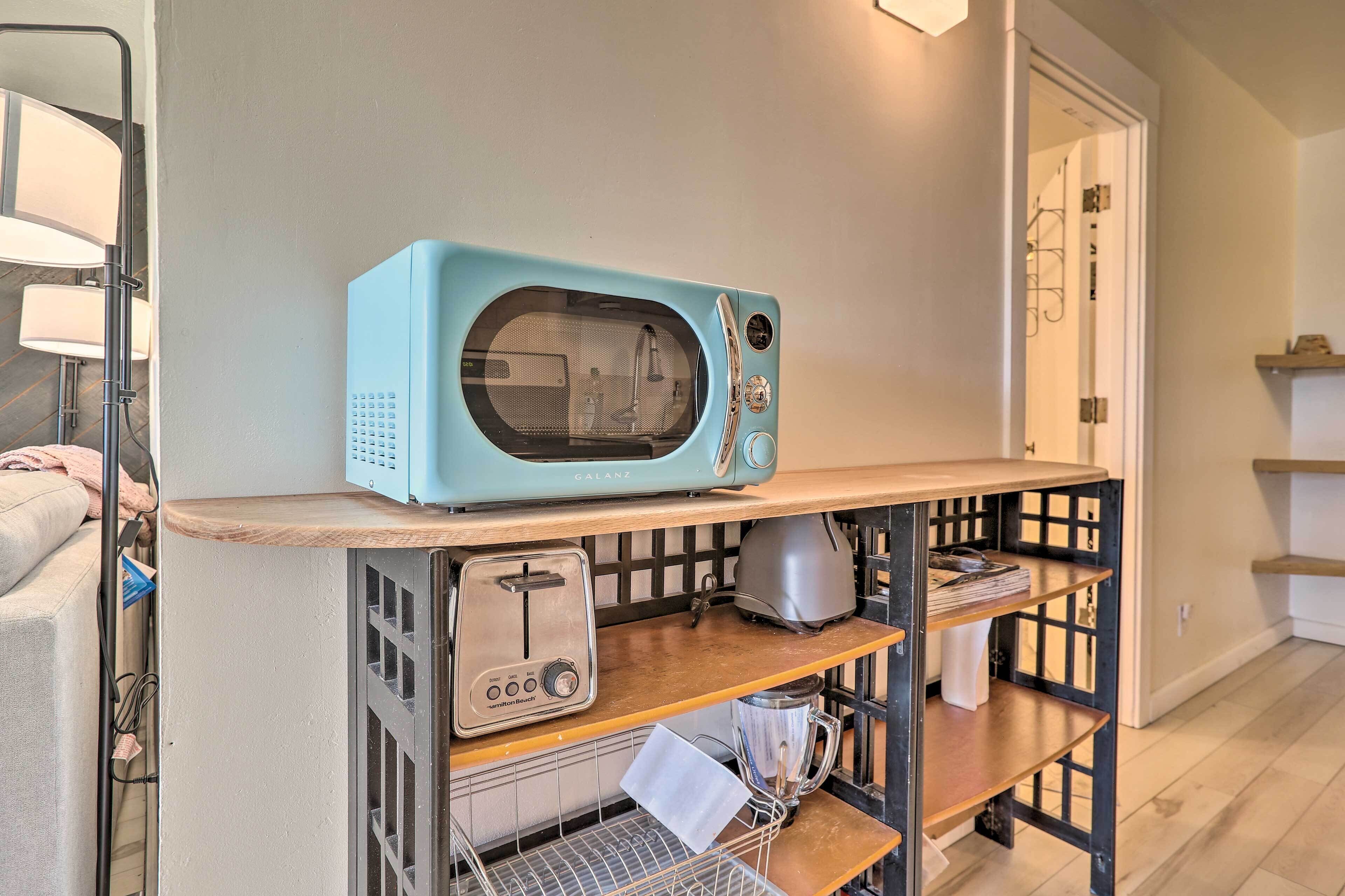A kitchen area with a blue microwave on a shelf, a toaster, a blender, and a kettle.