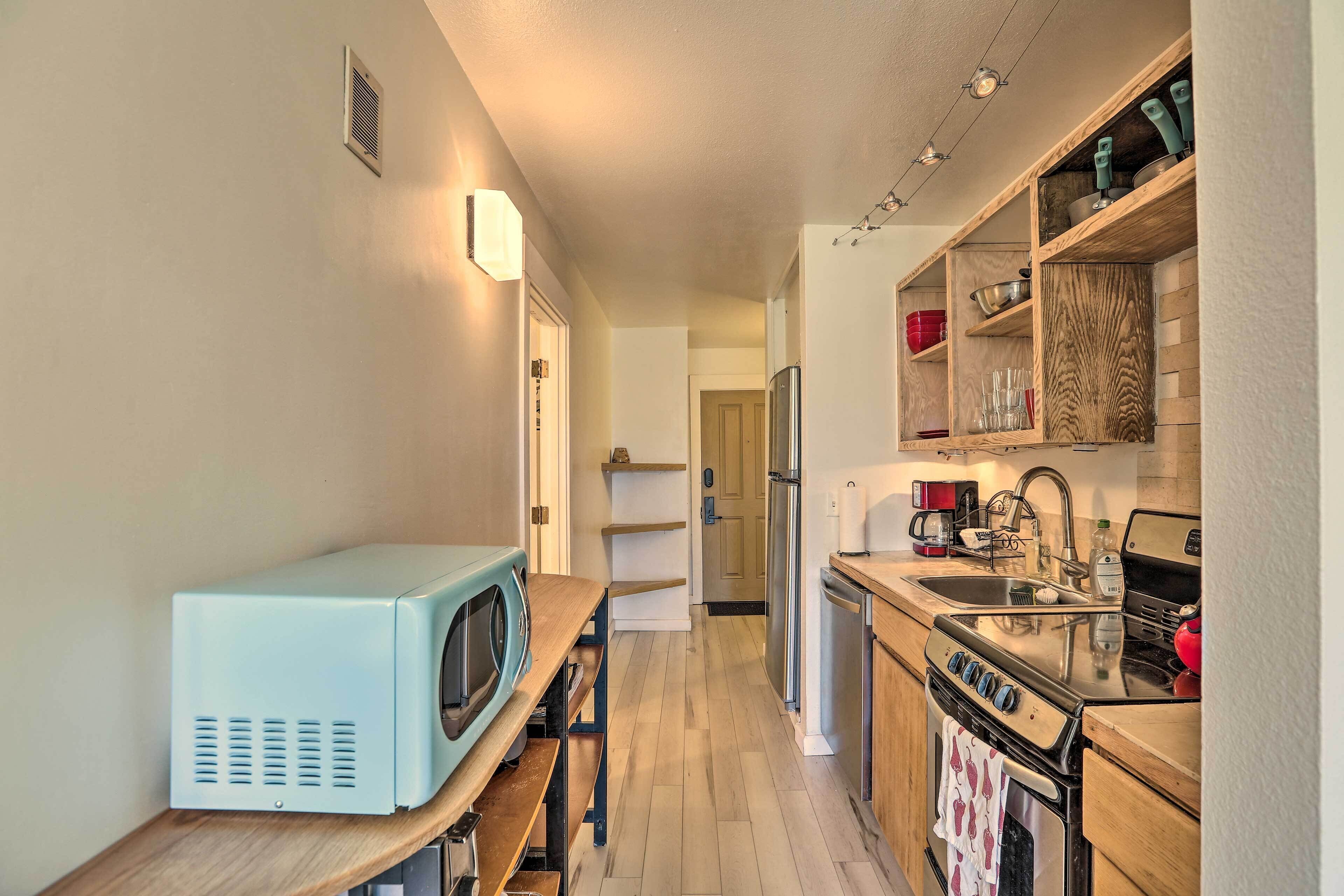 A narrow kitchen with a microwave, stove, refrigerator, and wooden shelves.