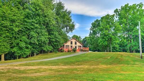 A two-story house with a red roof, surrounded by lush green trees and a well-maintained lawn. - Ohio River Views: Home w/ Fireplace & Deck! (Wolf Creek)