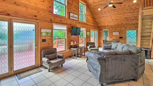 A wooden cabin interior with a sofa, armchairs, a TV, and a dining area. - Ohio River Views: Home w/ Fireplace & Deck! (Wolf Creek)