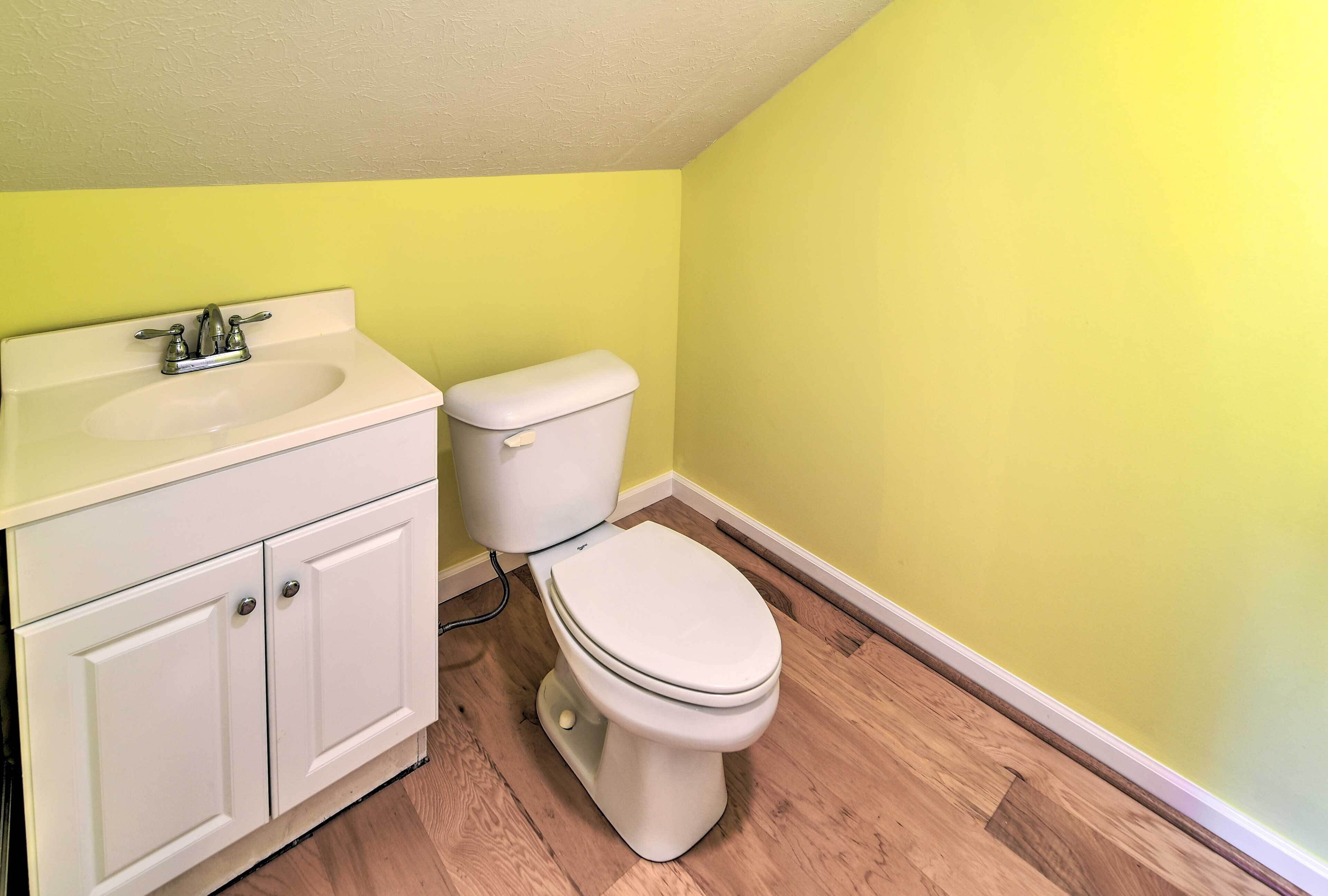 A bathroom with a white sink, cabinet, and toilet against a yellow wall.