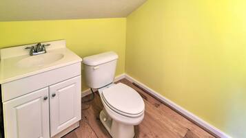 A bathroom with a white sink, cabinet, and toilet against a yellow wall.