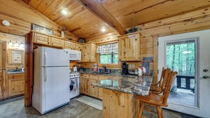 Une cuisine rustique, située dans une cabane en bois, équipée d’un réfrigérateur, d’une cuisinière et de meubles de rangement en bois.