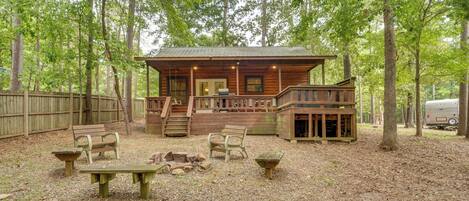 Un chalet rustique doté d’une véranda, de bancs en bois et d’une table de pique-nique, situé dans un espace boisé.