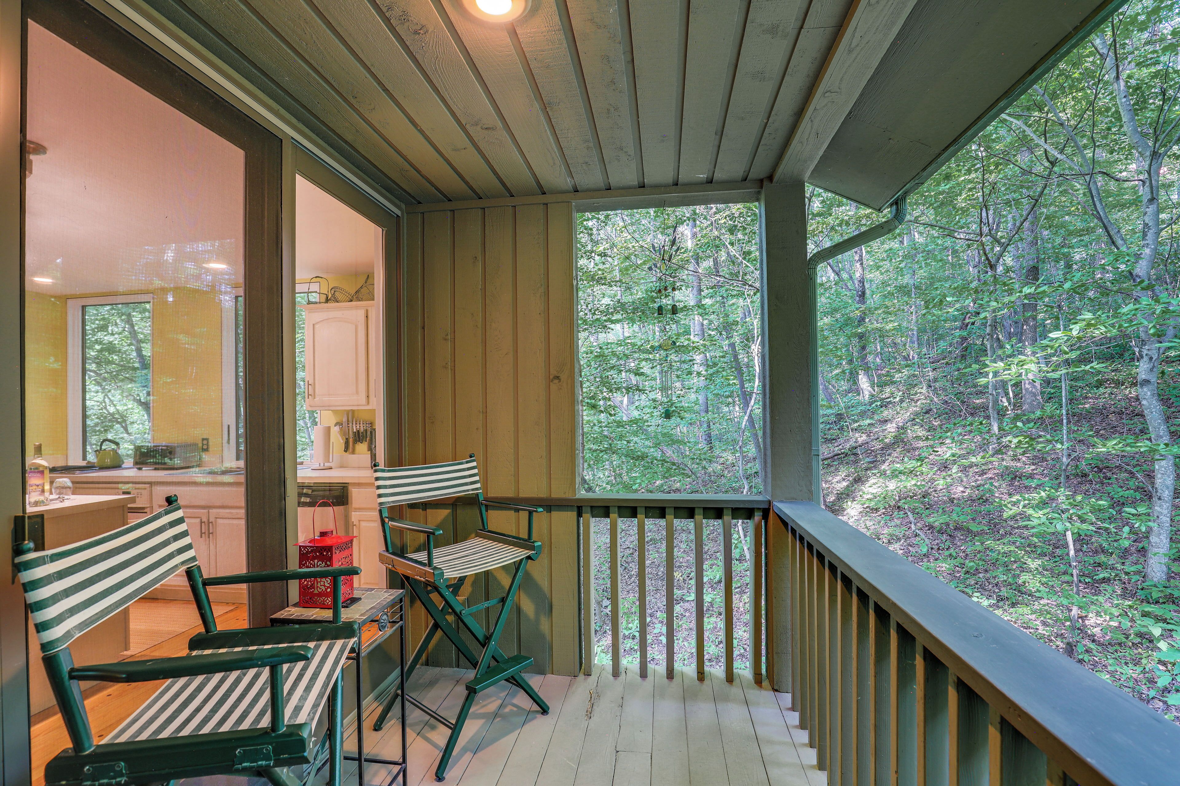 A wooden deck with a railing, a dining table with chairs, and a view of a forest.