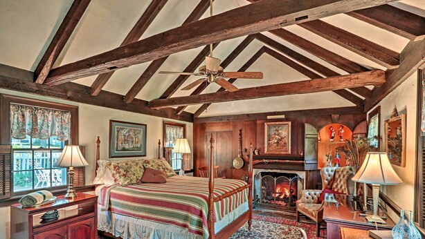 Une chambre à coucher de style traditionnel, avec un lit à baldaquin, des poutres apparentes, une cheminée et un lustre classique.