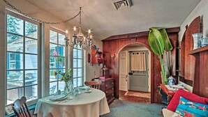 Un coin repas avec une table ronde, des chaises et un lustre. Une grande fenêtre à carreaux offre une vue sur l’extérieur.