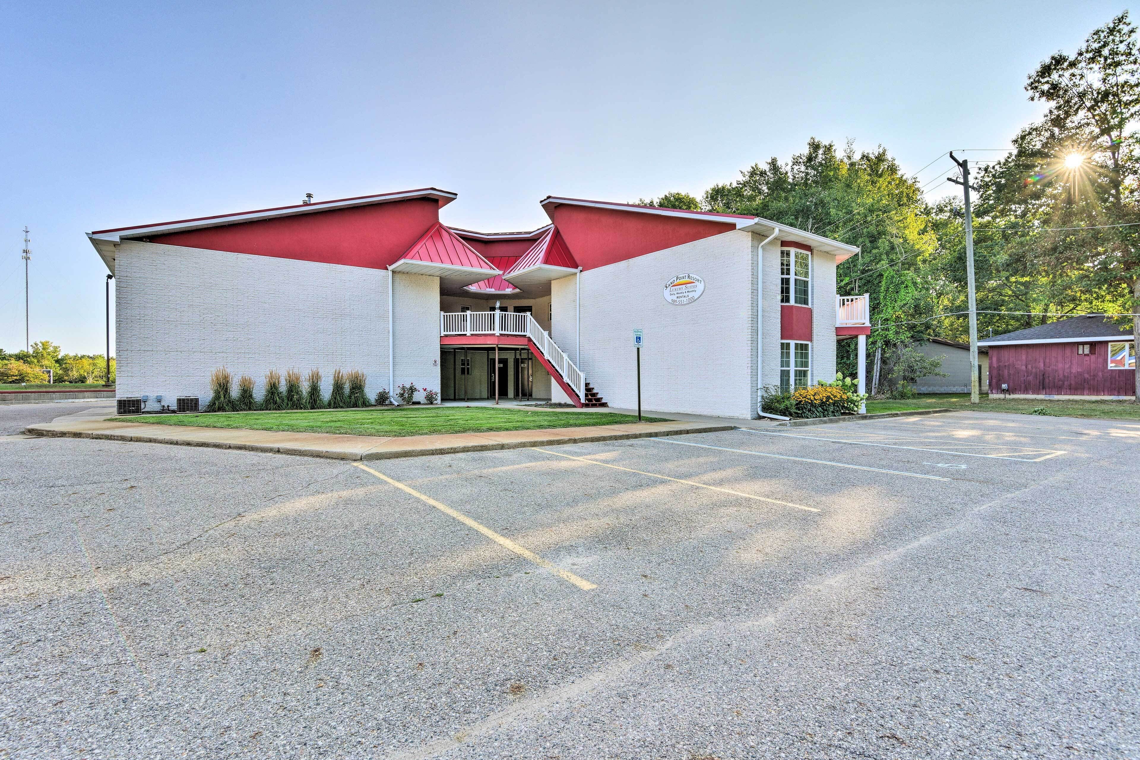 A building with a red and white facade, a central entrance with a staircase, and a parking lot in front.