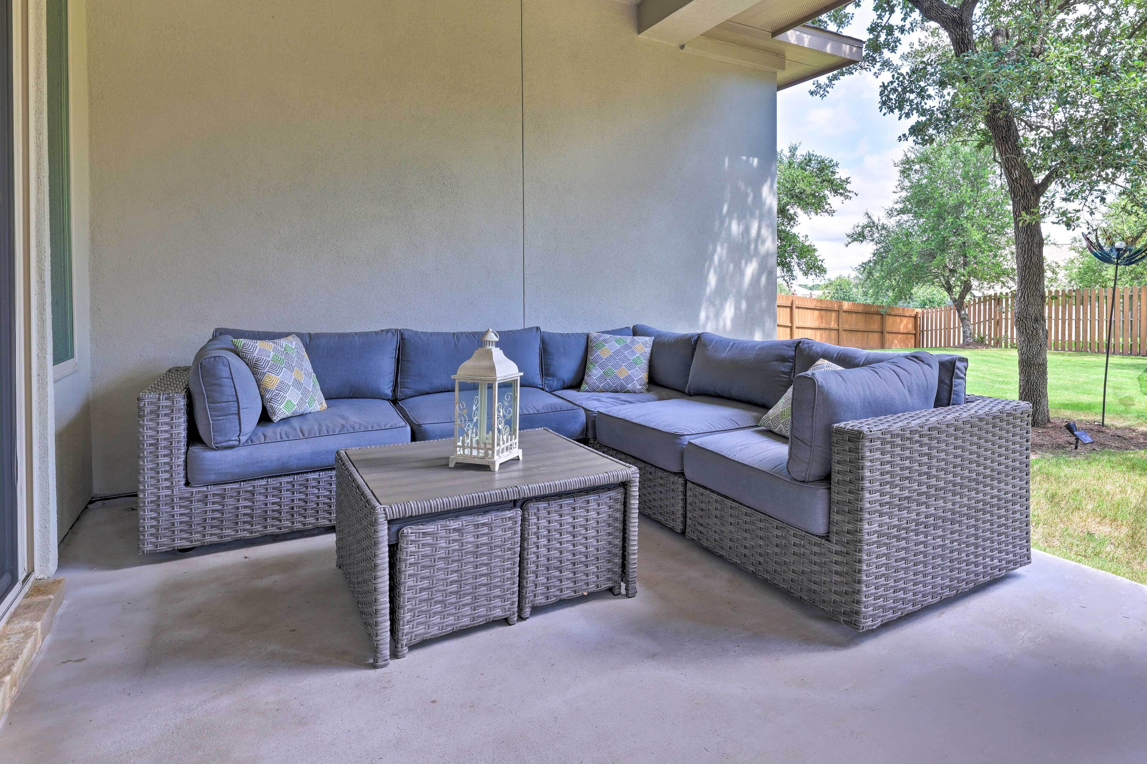 A covered patio area with a sectional sofa and a small table, featuring a lantern and a view of the backyard.