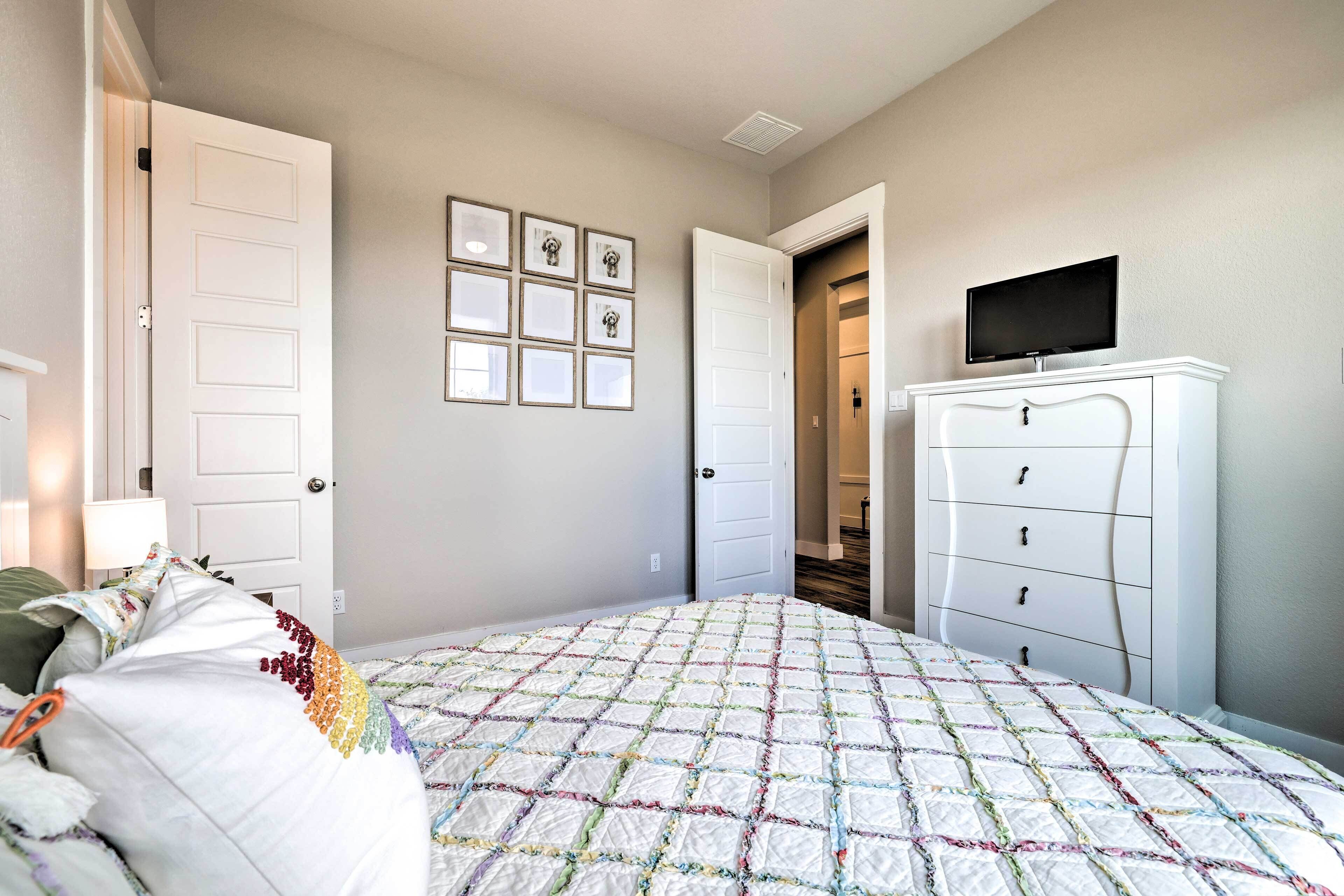 A bedroom with a quilted bedspread, a dresser, a television on top, and framed pictures on the wall.