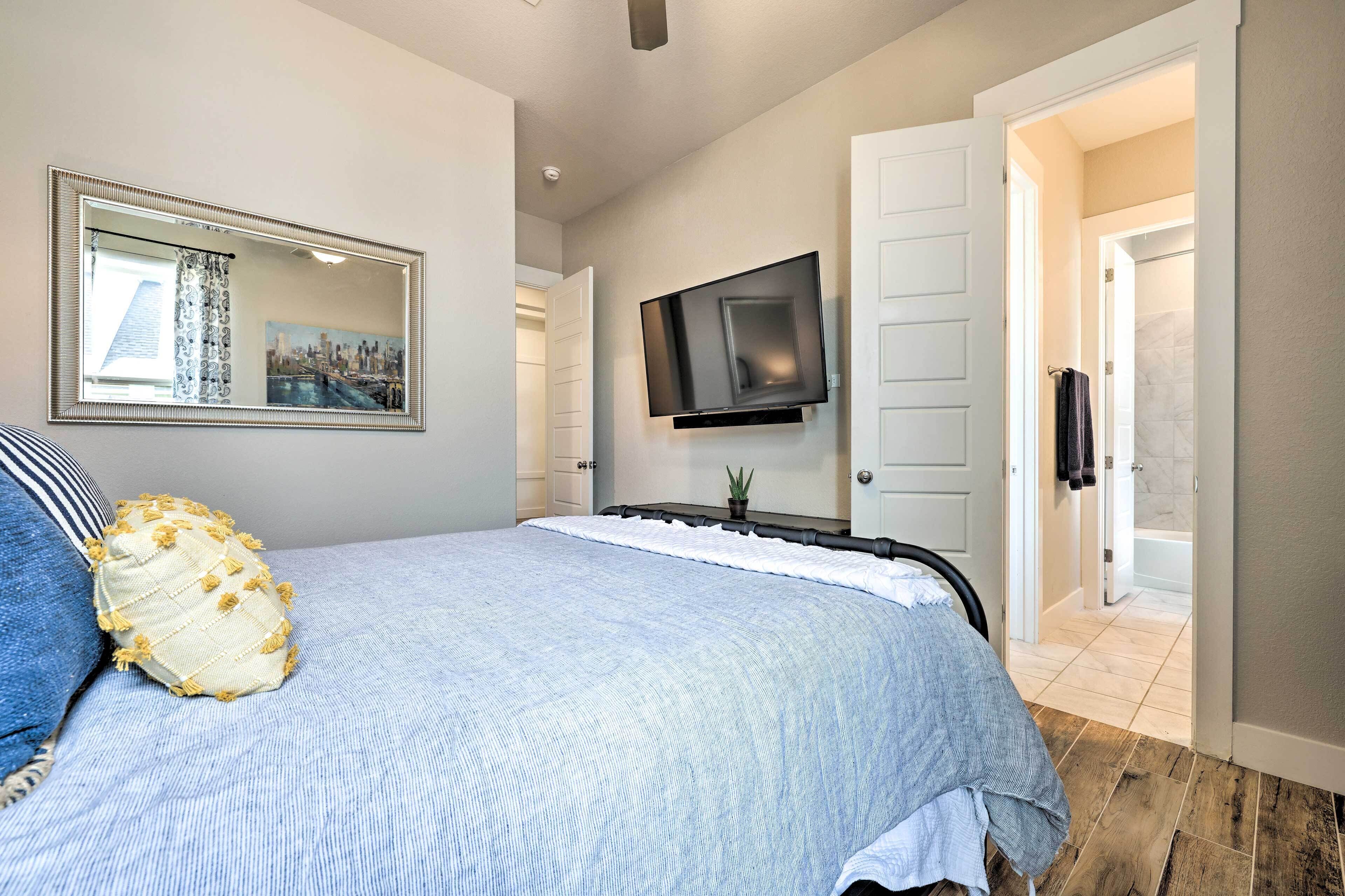 Un dormitorio con cama, un espejo grande, un televisor de pantalla plana y una puerta que da a un baño.