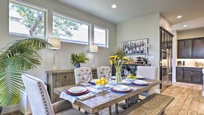 A dining area with a wooden table set for six, surrounded by upholstered chairs. There is a large window with a view of trees, a lamp, and a vase with flowers on the table. - Upscale Austin Area Escape: Families Welcome! (Austin)