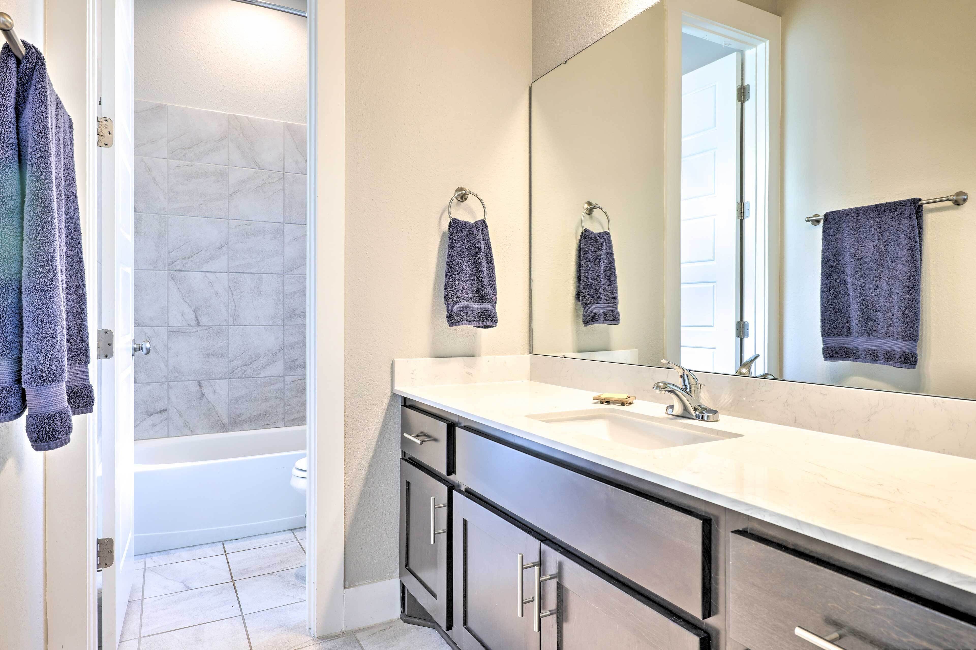 A modern bathroom with a bathtub, a large mirror, and a vanity with a sink.
