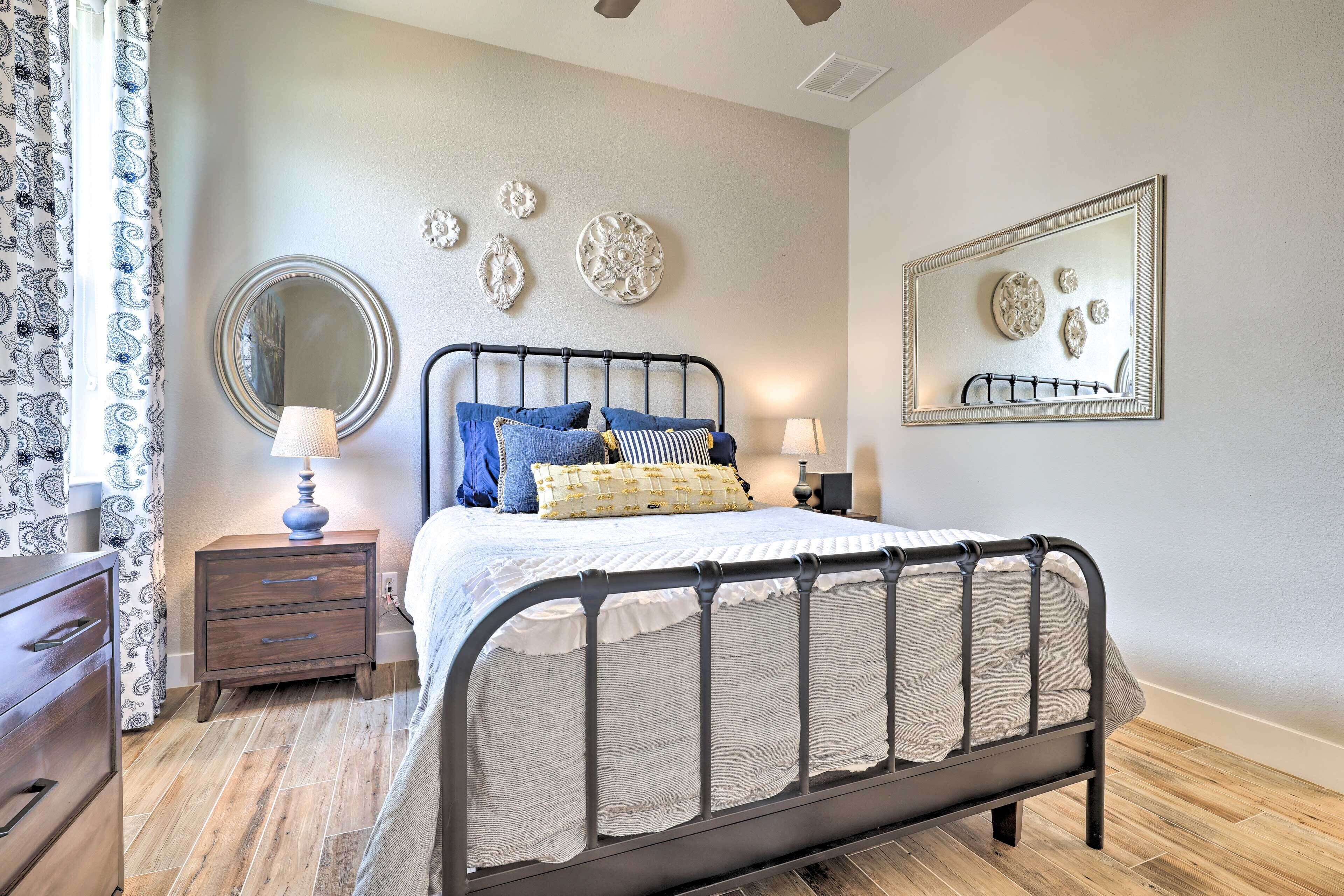 Une chambre à coucher avec un lit en métal, une table de chevet avec une lampe, une commode et des œuvres d’art décoratives au mur.