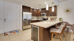 A modern kitchen with wooden cabinets, stainless steel appliances, and a central island with bar stools. - Mid-century Modern Phoenix Condo, Walk to High St! (Phoenix)