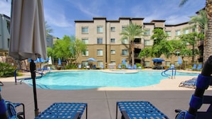 A pool area with lounge chairs and umbrellas, surrounded by a building with multiple floors and balconies. - Mid-century Modern Phoenix Condo, Walk to High St! (Phoenix)