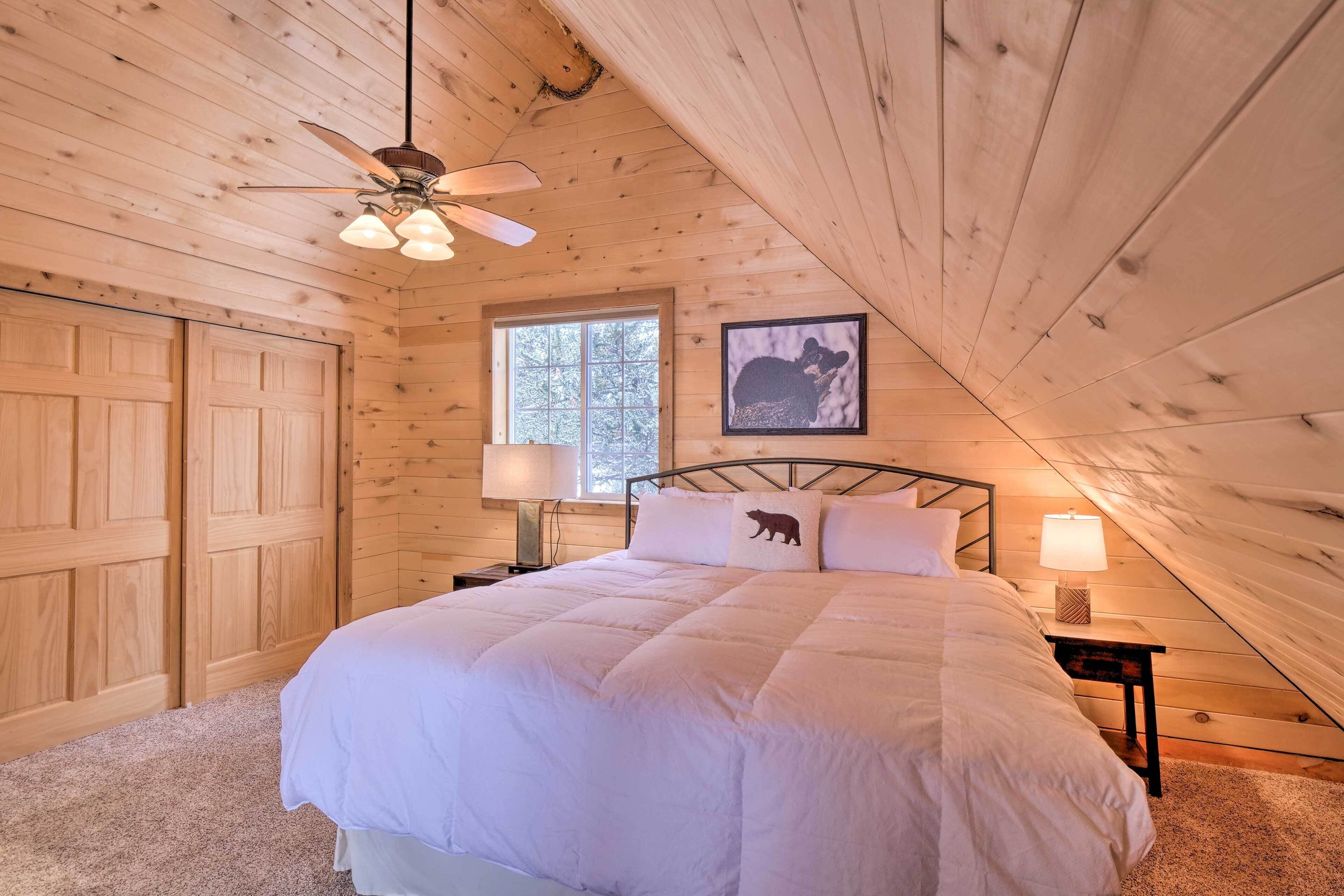 A cozy bedroom with a large bed, wooden walls, a ceiling fan, and a window.